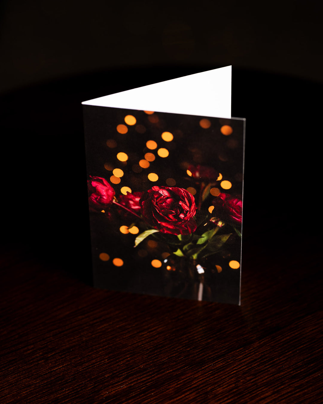 Red peonies with christmas lights in the background on the front of a blank card